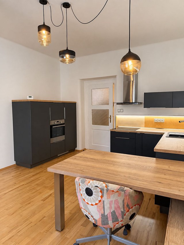 Obytná místnost s kuchyňskou linkou, jídelním stolem a designovými závěsnými svítidly